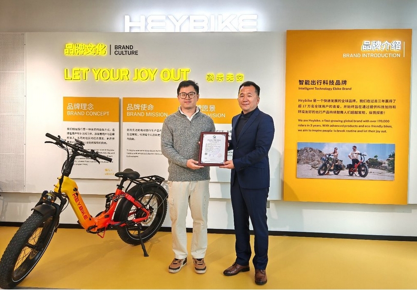 Two men standing in front of a yellow and orange signDescription automatically generated